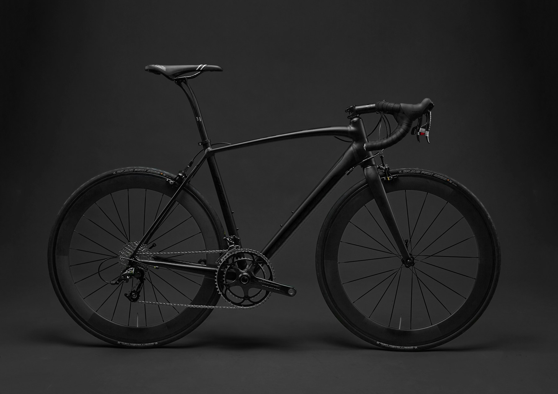 Black road bike in profile against a dark studio background